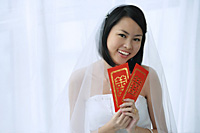 A bride smiles at the camera and holds out two red envelopes - Asia Images Group