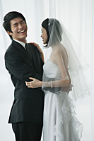 A newlywed couple stand with their arms around each other - Asia Images Group