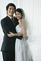 A newlywed couple hug and smile at the camera - Asia Images Group