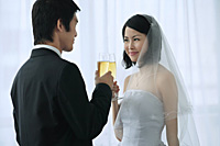 A newlywed couple hold out their champagne glasses for a toast - Asia Images Group