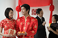 A newlywed couple smile at each other as their family talk in the background - Asia Images Group