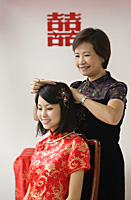 A bride sits down as her mother combs her hair - Asia Images Group