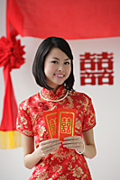 A bride smiles as she holds two red envelopes - Asia Images Group