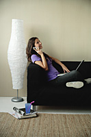 A teenage girl sits on the couch and talks on the phone - Asia Images Group