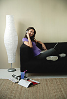 A teenage girl sits on the couch and talks on the phone - Asia Images Group