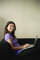 A teenage girl smiles at the camera as she uses a laptop - Asia Images Group