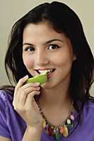 A teenage girl looks at the camera as she eats a piece of fruit - Asia Images Group