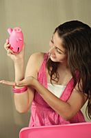 A teenage girl tries to get money from a piggy bank - Asia Images Group