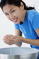 A young woman smiles at the camera as she washes her face - Asia Images Group