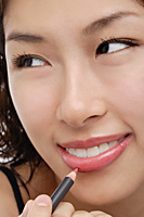 A young woman applies lip pencil - Asia Images Group