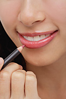 A young woman applies lip pencil - Asia Images Group
