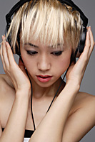 A young woman with headphones on listens to music - Asia Images Group