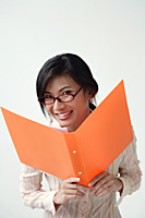 A woman smiles at the camera as she holds an orange folder - Asia Images Group