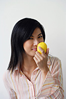 A woman looks at the camera as she holds up a lemon - Asia Images Group