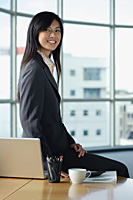 A woman smiles at the camera as she sits on her desk - Asia Images Group