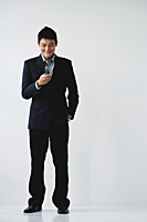 A man wearing a suit smiles as he dials on his cellphone - Asia Images Group