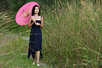 Woman walking in long grass with parasol - Asia Images Group