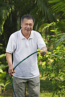 Man with hose, watering garden - Asia Images Group