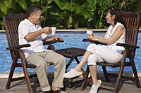Couple relaxing in deck chairs by the pool, having tea - Asia Images Group
