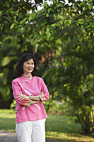 Woman standing, arms crossed, in park - Asia Images Group