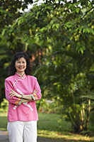 Woman standing, arms crossed, in park - Asia Images Group