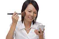 Woman applying make-up  while looking into compact mirror - Asia Images Group