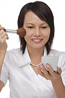 Woman applying cosmetics while looking into compact mirror - Asia Images Group