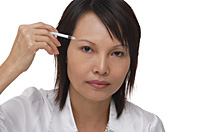 Woman applying make-up while looking at camera - Asia Images Group