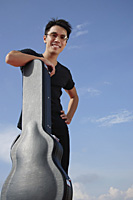 Man leaning against guitar case - Asia Images Group