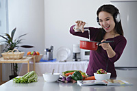 Young woman cooking while listening to music - Asia Images Group