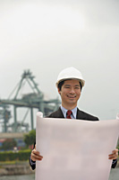 Engineer with plans and hard helmet looking at camera - Asia Images Group