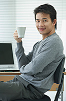Man with cup relaxing at desk and looking at camera - Asia Images Group