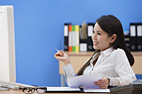 Businesswoman sitting at desk and looking at computer screen - Asia Images Group