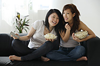 Young women enjoying popcorn on couch - Asia Images Group
