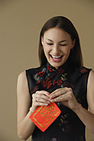Young woman laughing while opening red envelope - Asia Images Group