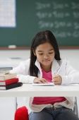 Girl writing and sitting at school desk - Asia Images Group