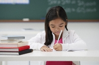 Girl writing and sitting at school desk - Asia Images Group