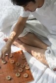 Young man sitting on bed, playing chinese chess - Asia Images Group