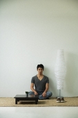 Serious young man sitting on floor, looking at camera - Asia Images Group