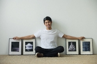 Young man sitting on floor surrounded by framed photographs - Asia Images Group