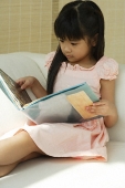 Little girl sitting on sofa reading book - Asia Images Group