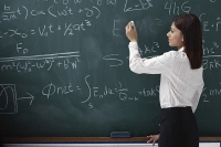 Woman writing equations on chalk board - Asia Images Group