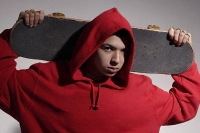young man wearing red hooded sweatshirt holding skateboard - Asia Images Group