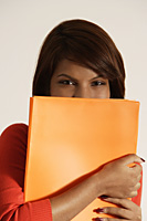 Business woman holding a orange work file in front of her face - Asia Images Group