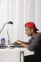 young man with red cap working on laptop - Asia Images Group
