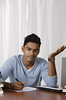 young man writing at his desk, puzzled - Asia Images Group