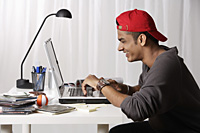 young man with red cap working on laptop - Asia Images Group