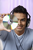 young man with headphones on, holding compact disc in front of him - Asia Images Group
