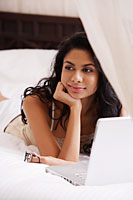 Indian woman laying on bed smiling with laptop - Asia Images Group