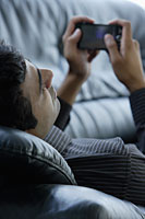 Indian man laying on black sofa surfing on phone. - Asia Images Group